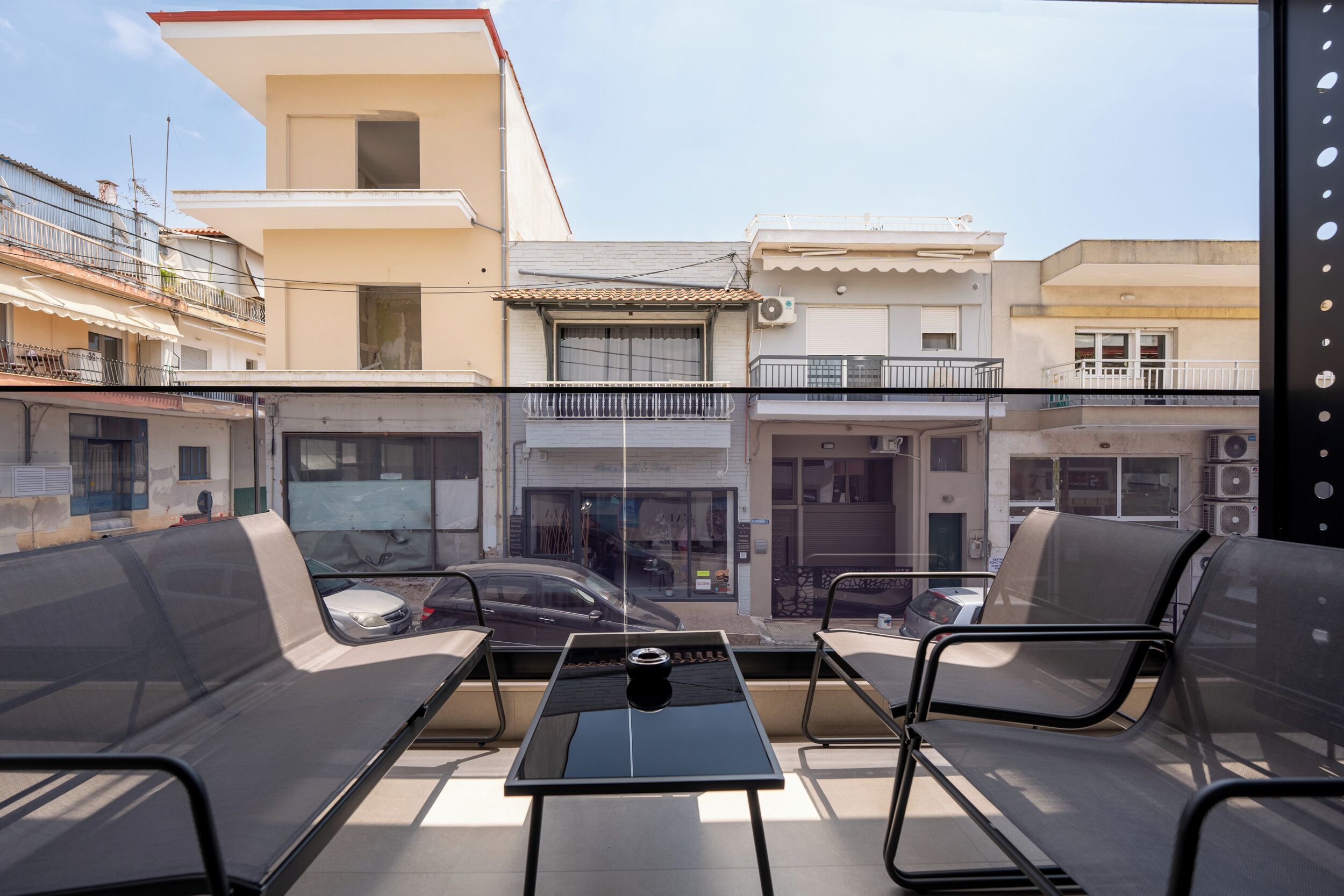An outdoor seating area with chairs and a table, overlooking a street with buildings and parked cars.