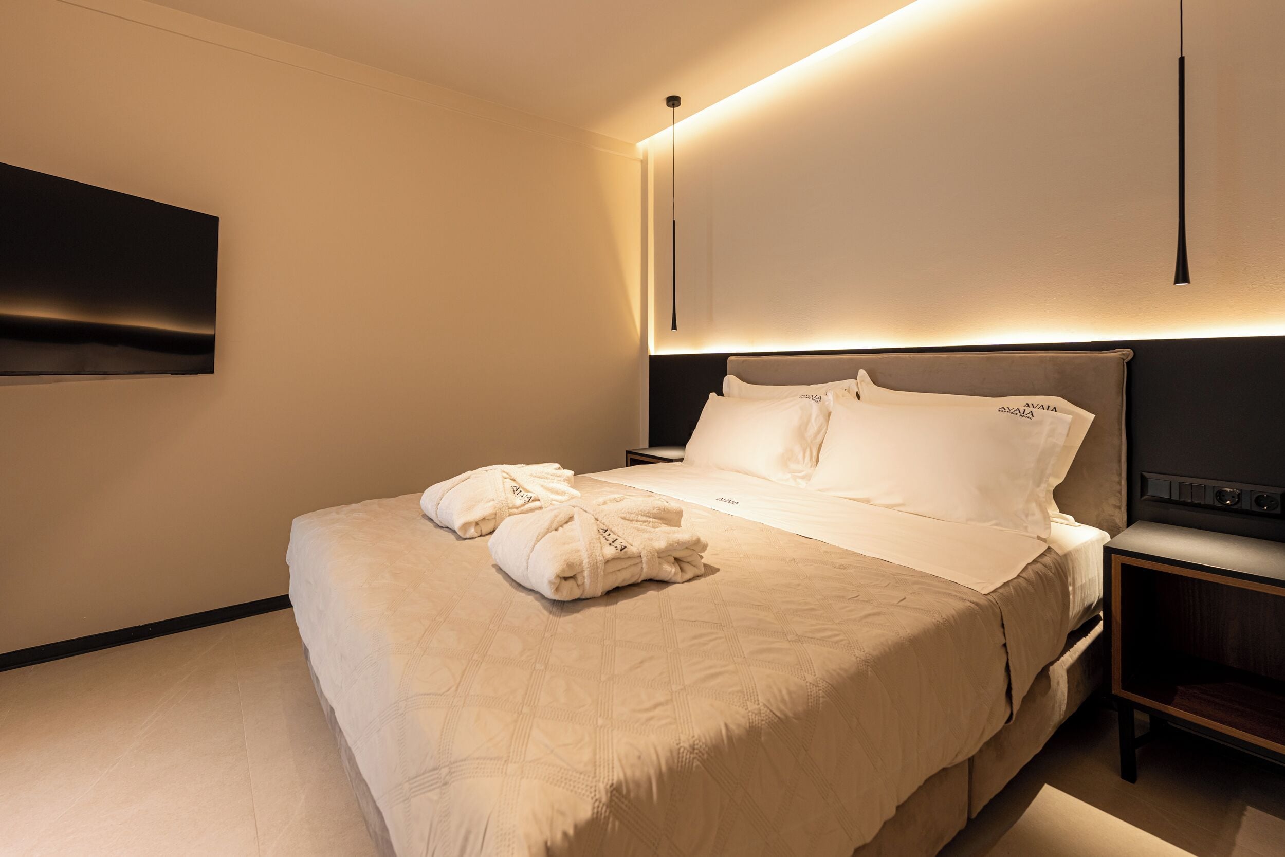 Un letto rifatto con cura, un comodino e una TV a parete.