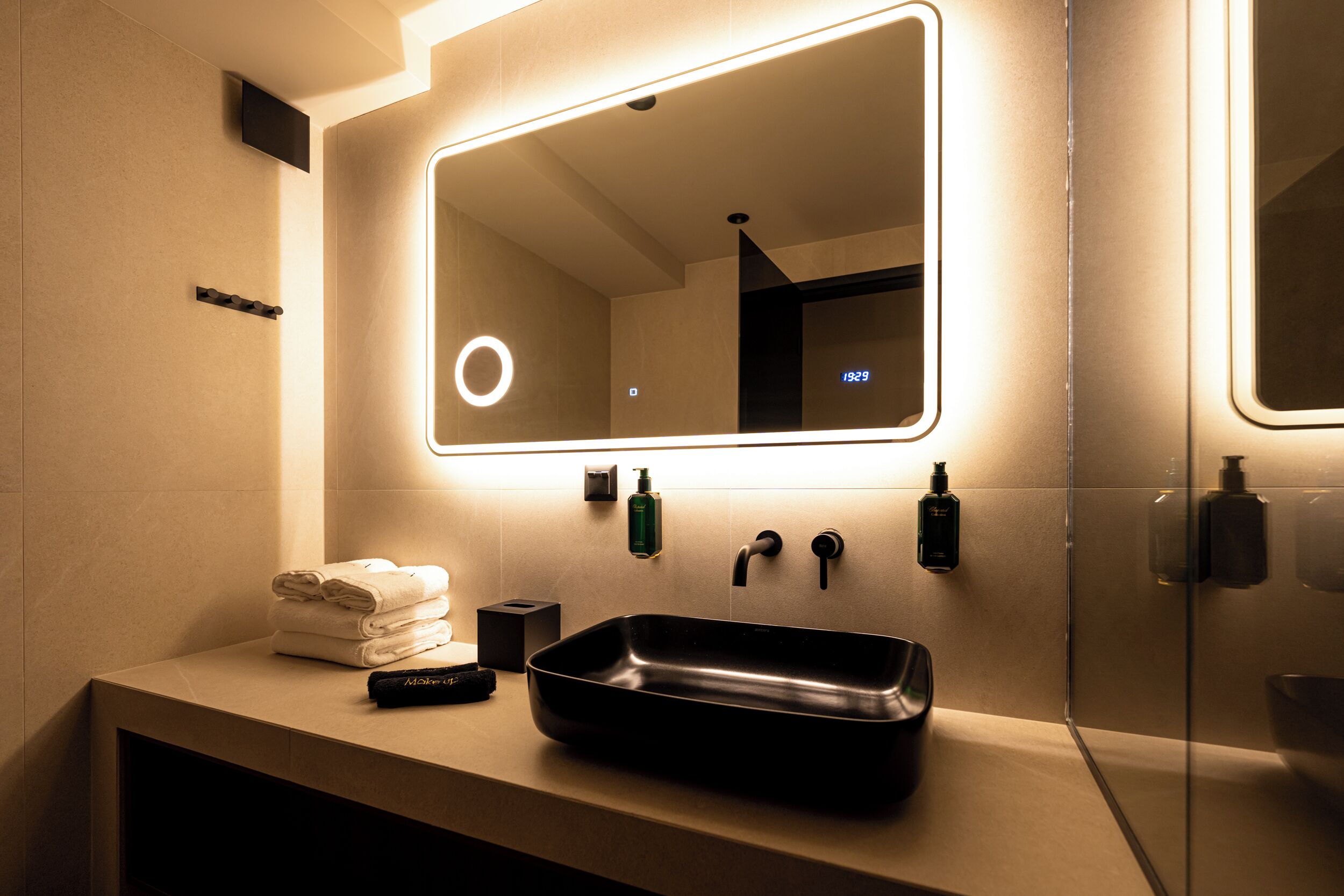 A modern bathroom with a large mirror, a black sink, and neatly folded towels.
