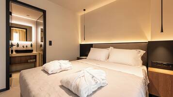 A hotel room with a bed, a bedside table, a nightstand, a mirror, and a bathroom vanity.