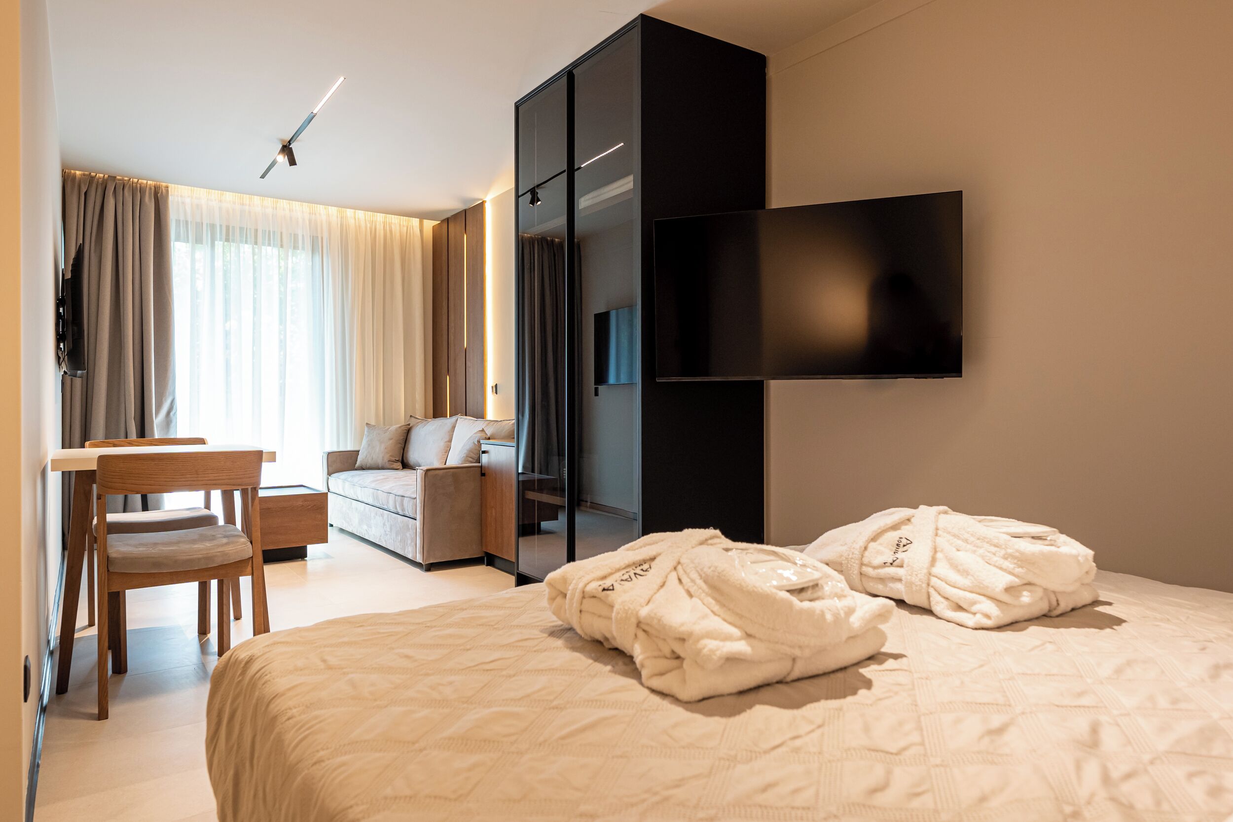 Hotellihuone, jossa on sänky, työpöytä, tuoli, sohva, seinälle asennettu televisio ja vaatekaappi.