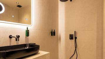 A modern bathroom with a large mirror, a black basin, a showerhead, and two bottles of shampoo on the wall.