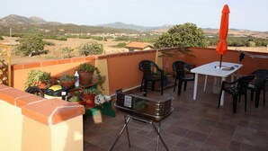 Un patio con mesa, sillas, una sombrilla y plantas en macetas.