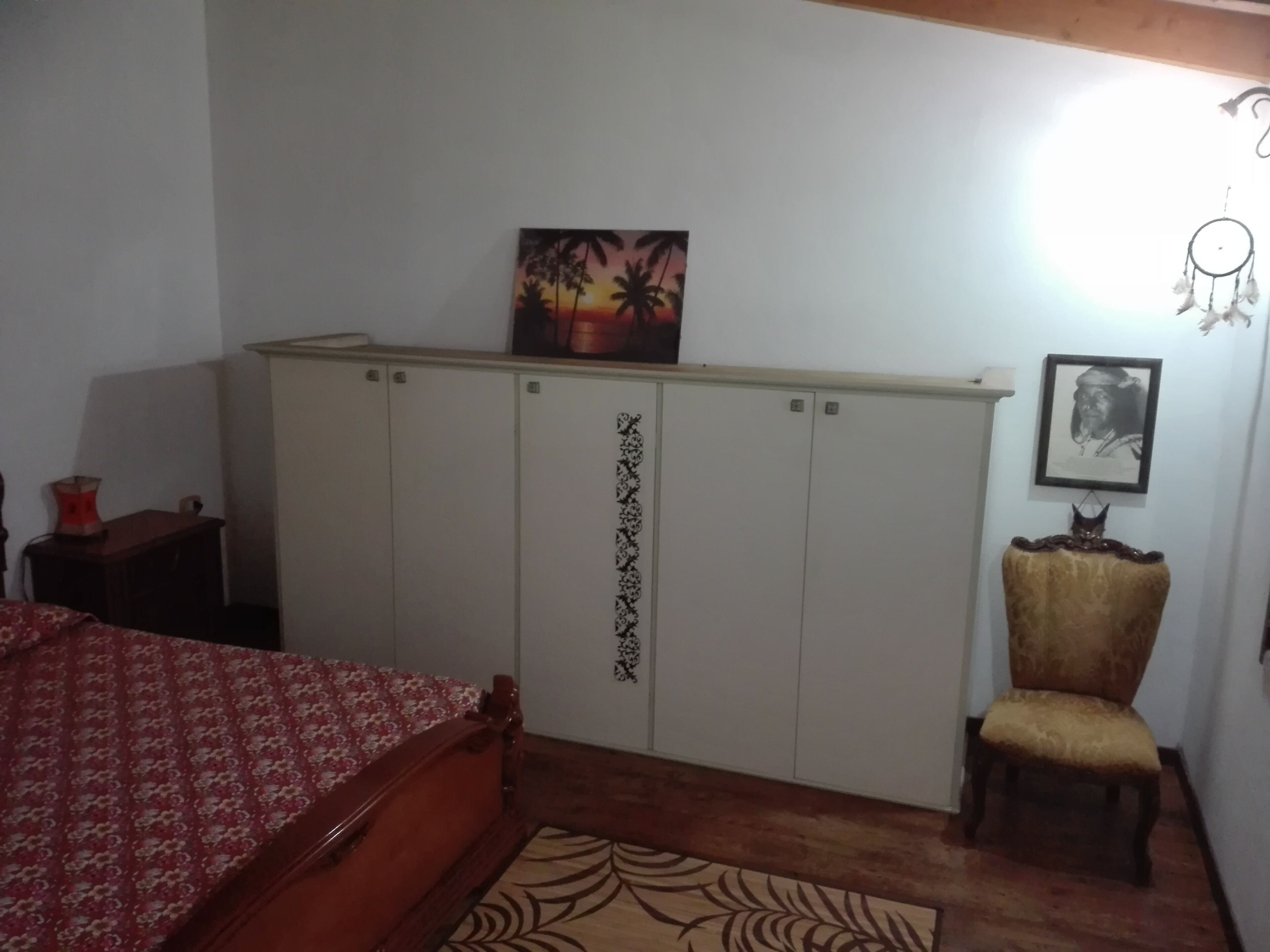 A bedroom with a bed, a wardrobe, a chair, and a wall-mounted picture.