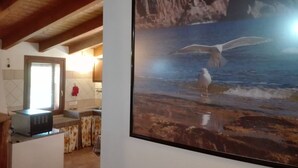 Una habitación con área de cocina, una puerta y un cuadro con una gaviota en la pared.
