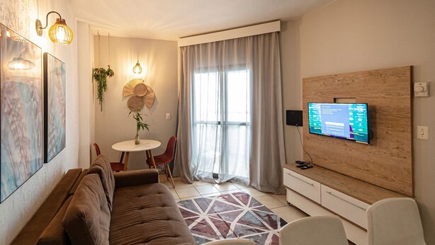 A modern living room with a brown sofa, a white coffee table, and a TV mounted on a wooden wall. - SHB Apartamento Com Vista ao Mar (Santos)