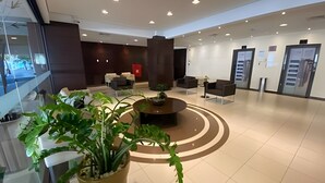 A modern lobby with a central seating area, a reception desk, and a large potted plant. - SHB Apartamento Com Vista ao Mar (Santos)