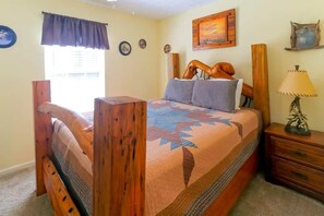 A wooden bed with a quilt, a nightstand with a lamp, and a window with curtains. - The Big Bear Retreat in Helen (Helen)