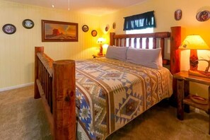 A bedroom with a wooden bed, a patterned bedspread, a nightstand with a lamp, and wall decorations. - The Big Bear Retreat in Helen (Helen)