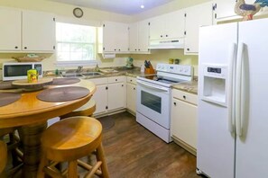 Een keuken met witte kastjes, een magnetron, een fornuis en een koelkast.