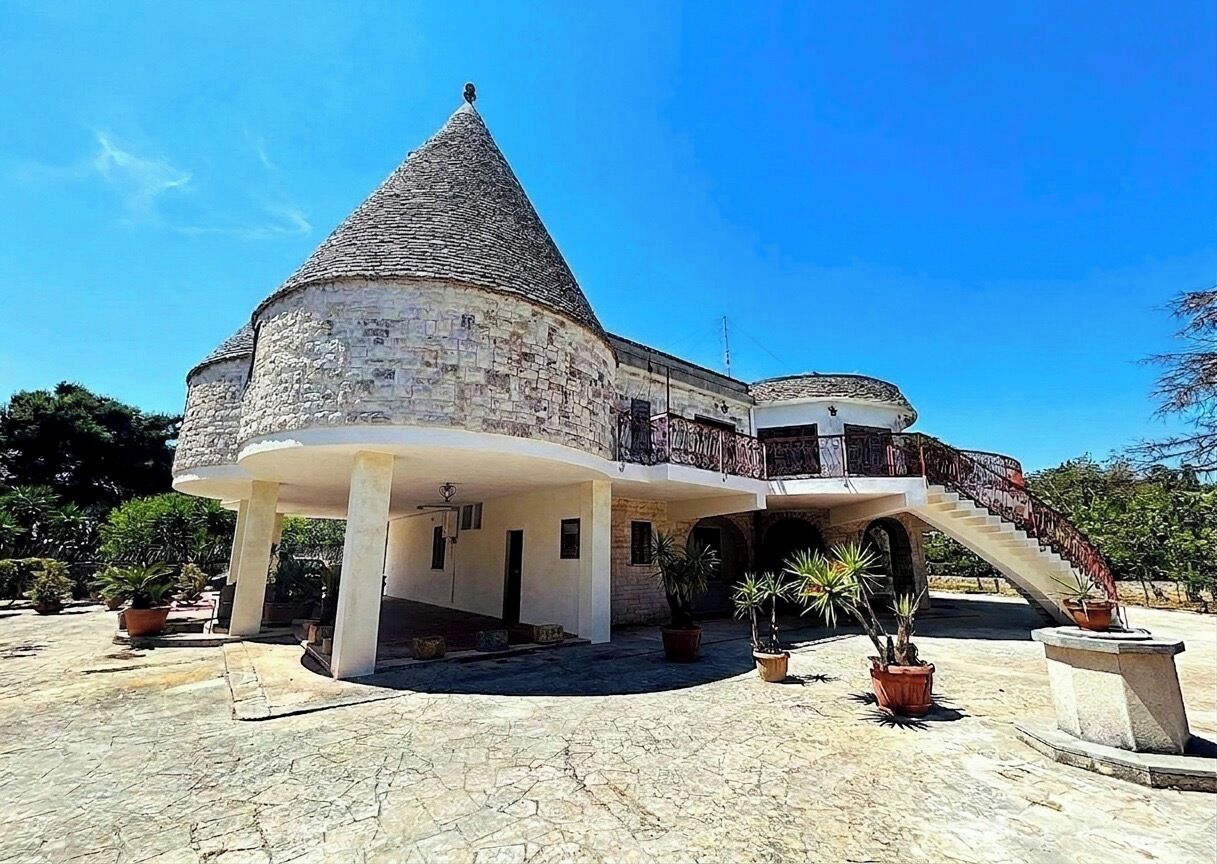 Ein Steinhaus mit einem Kegeldach, einem Balkon und einer Treppe, die zu einer oberen Ebene führt.
