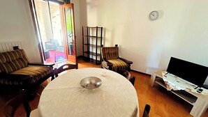 Ein Wohnzimmer mit rundem Tisch, Fernseher, Bücherregal und einem Sessel.