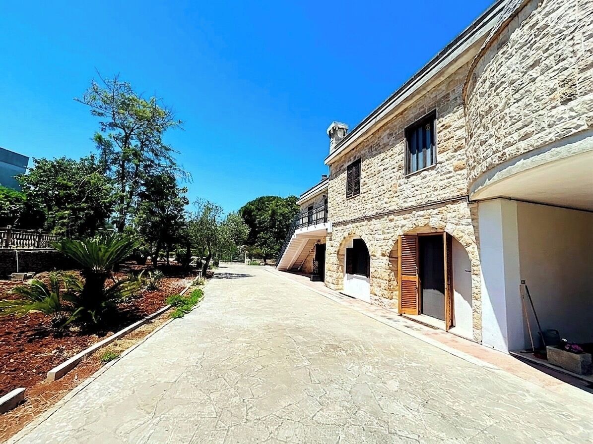 Un edificio de piedra con camino pavimentado, arcos en las entradas y cielo azul despejado.
