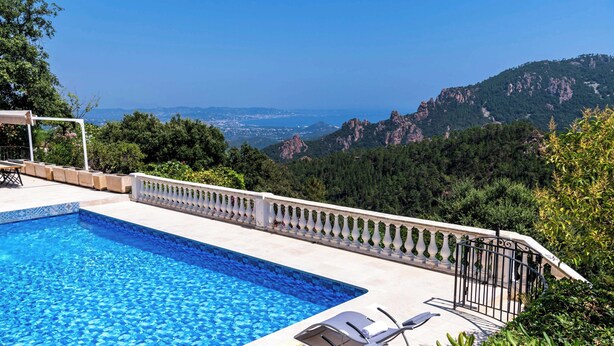 Piscina com vista para montanhas, cerca branca e algumas cadeiras de descanso.
