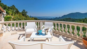 Um terraço com cadeiras brancas e uma mesa, vista da paisagem e céu claro.