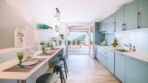 Uma cozinha moderna com uma ilha central, banquetas e vista para uma área de refeições ao ar livre.