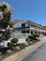 Un motel con un cartel de 'WELCOME', un estacionamiento cercado y un jardín bien cuidado.