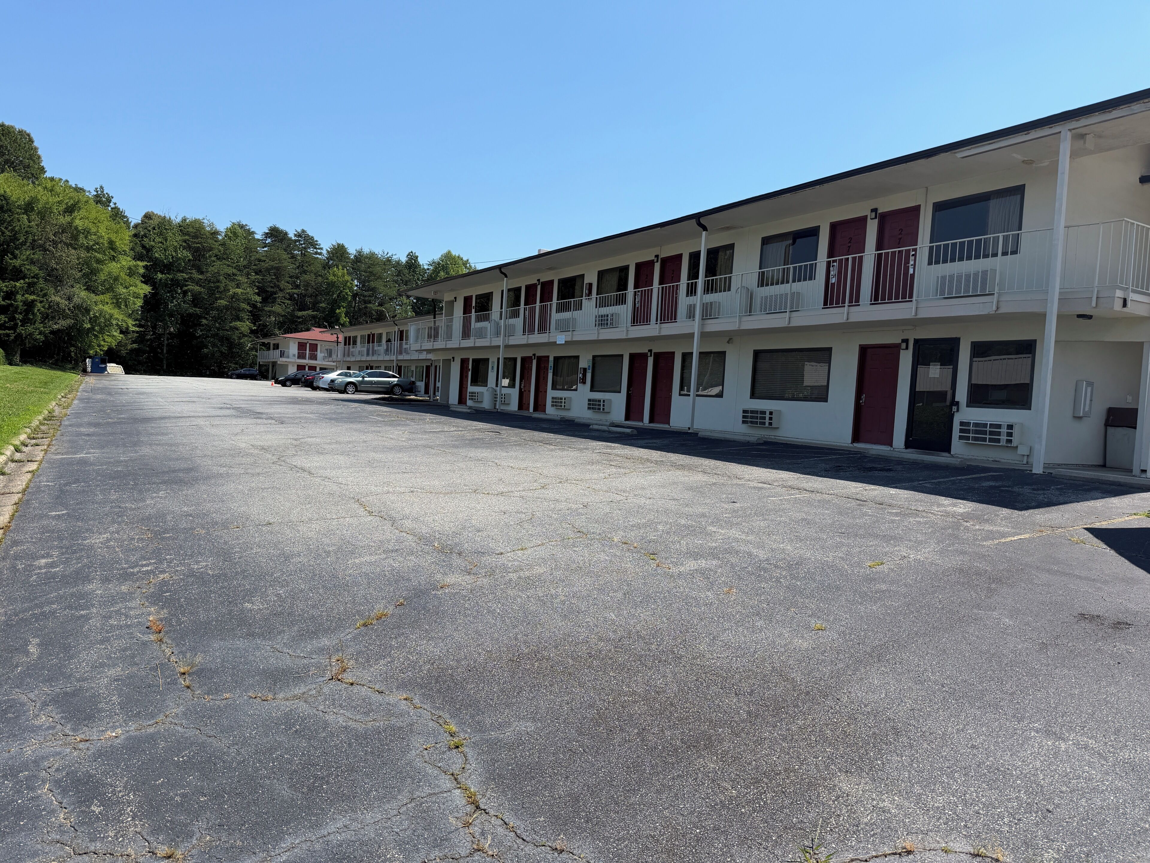 A motel with multiple rooms, a parking lot, and a green area with trees.