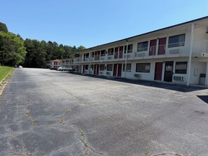 A motel with multiple rooms, a parking lot, and a green area with trees. - Travel Inn (Greensboro)