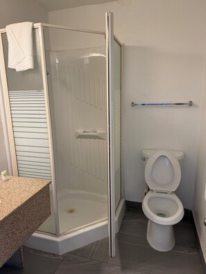 A bathroom with a glass-enclosed shower, a toilet, and a granite countertop. - Travel Inn (Greensboro)
