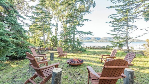 Eine Terrasse mit Adirondack-Stühlen, einer Feuerstelle und Blick auf einen See und Berge.