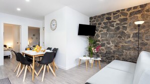Ein modernes Wohnzimmer mit Steinwand, einem Flachbildfernseher, einer Essecke mit Tisch und Stühlen und einem weißen Sofa.