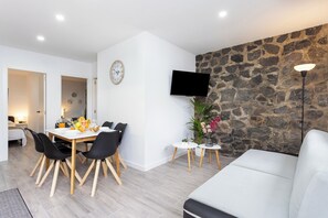 A modern living room with a stone wall, a flat-screen TV, a dining area with a table and chairs, and a white sofa. - TenoHomes Sunny Terrace & Private Pool (Icod de los Vinos)