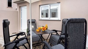Eine Terrasse mit Tisch, Stühlen, einer Obstschale und einem Fenster.