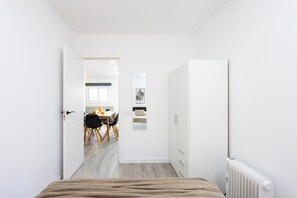 A modern, minimalist bedroom with a large bed, a radiator, and a view into a dining area with a table and chairs. - TenoHomes Sunny Terrace & Private Pool (Icod de los Vinos)