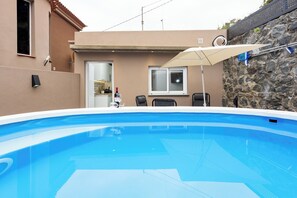 A swimming pool with a stone wall and a door leading to a kitchen.