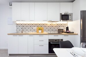 A modern kitchen with white cabinets, a microwave, a sink, and a dining area with a table set for two.