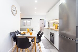 A modern kitchen with a stainless steel refrigerator, a dining table with black chairs, and a clock on the wall.