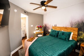 Ein Schlafzimmer mit einem Bett, einem Schminktisch mit Spiegel, einem Deckenventilator und einem Wandbild.