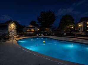 En swimmingpool om natten med et ur på en bygning, omgivet af huse og træer.
