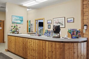Ein Empfangsschalter mit Holzoptik, gerahmte Kunstwerke an der Wand und eine Bärenskulptur.
