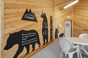 Ein Holzinnenraum mit einem an der Wand befestigten Schild, das 'Gatlingburg Summit' zeigt, einer Bärensilhouette und einem Tisch mit Stühlen.