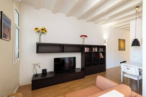A modern living room with a flat-screen TV, dark wooden entertainment unit, a pink sofa, and a dining area with a white table and chairs. - 23NO1138 - Apartment in Poble Sec (Barcelona)