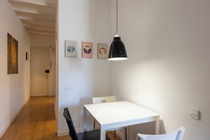 A room with a white table, a black chair, a hanging pendant light, and three framed pictures on the wall. - 23NO1138 - Apartment in Poble Sec (Barcelona)