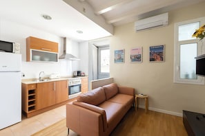 A compact living space with a kitchenette, a sofa, a small table, and wall-mounted artwork. - 23NO1138 - Apartment in Poble Sec (Barcelona)