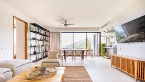 Ein modernes Wohnzimmer mit Sofa, Couchtisch, Bücherregal, Essbereich und Fernseher.