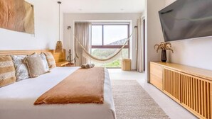 Ein Schlafzimmer mit einem großen Bett, einem Fernseher, einer Hängematte und Blick ins Freie.