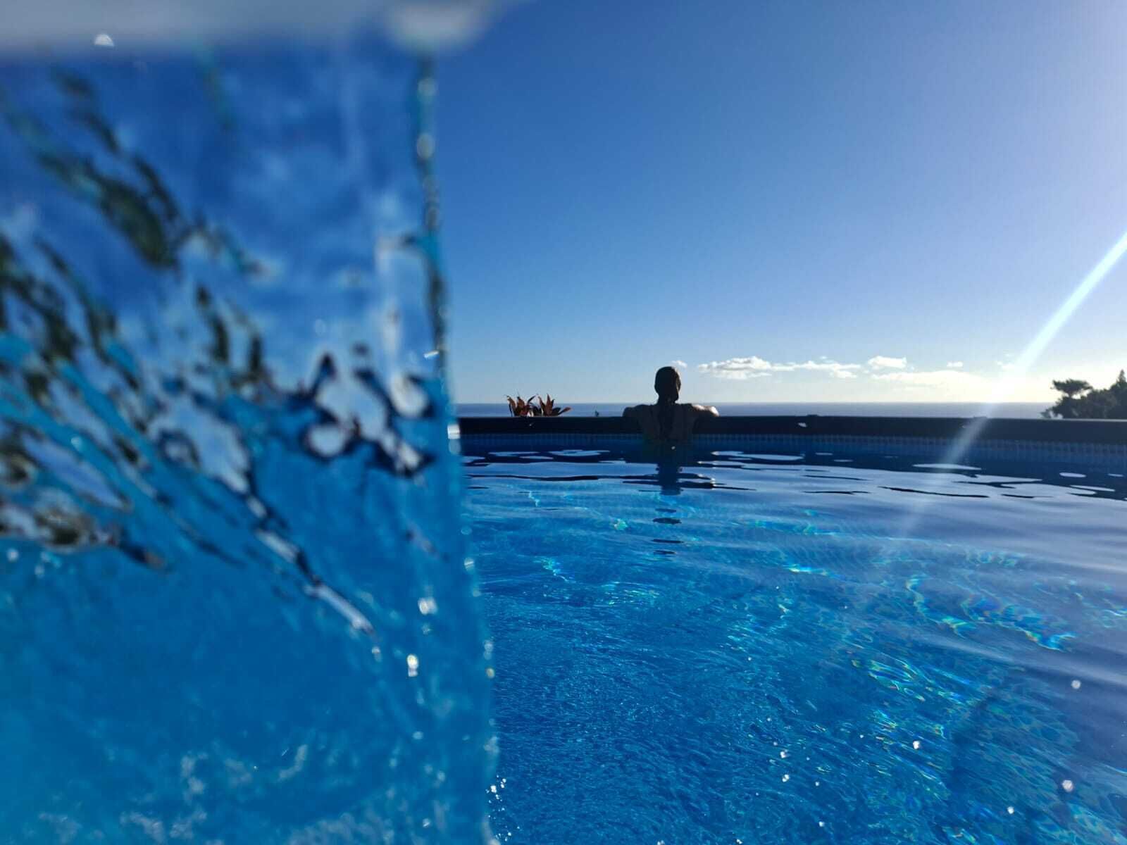 A clear view of a swimming pool with a person in the water, a clear sky, and a distant horizon.