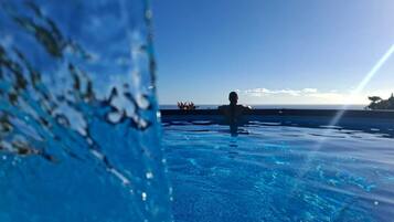 A clear view of a swimming pool with a person in the water, a clear sky, and a distant horizon.