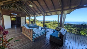 Una terraza de madera con un sofá y una mesa pequeña, barandilla de madera y vista al océano.