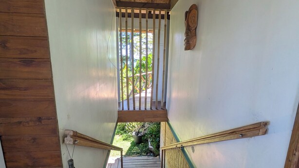 Una escalera de madera con barandilla de metal que conduce a un espacio exterior con vegetación.