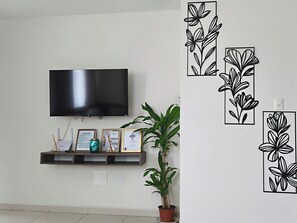 Ein Flachbildfernseher an der Wand, ein Regal mit gerahmten Zertifikaten, ein Blumentopf und Wanddekoration.