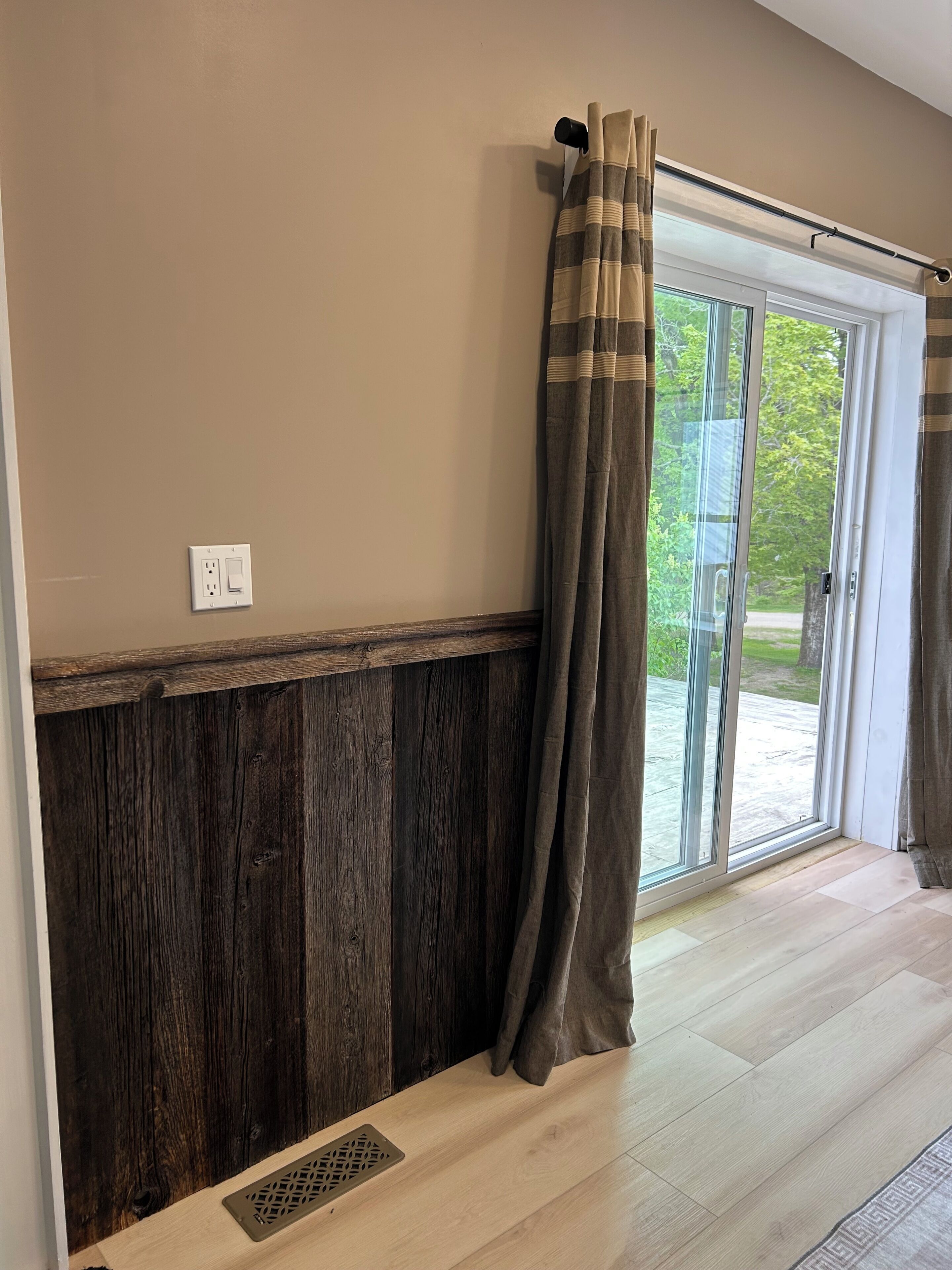 A room with a wooden wainscoting, a sliding glass door with curtains, and a visible electrical outlet.