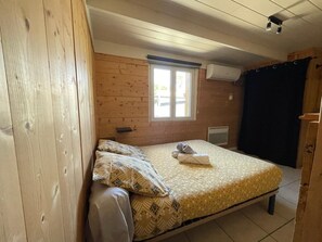 A single bed with a patterned bedspread, a window with blinds, and a wooden wall. - Beach House Next to the Current (Mimizan)