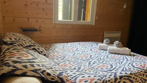 Ein Zimmer einer Holzhütte mit Bett, Kissen, einem Fenster und einer Heizung.