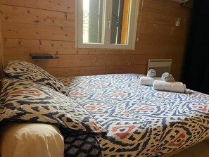 Ein Zimmer einer Holzhütte mit Bett, Kissen, einem Fenster und einer Heizung.
